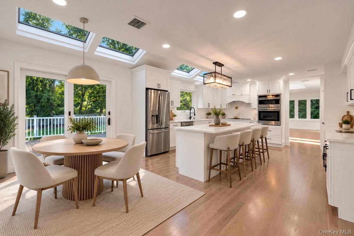 Kitchen featuring white cabinetry, center island with stone-finish countertops, stainless steel appliances, recessed skylights, and wood-finish floori