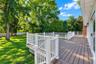 Raised composite deck with white railings, expansive grass lawn, mature trees, and white perimeter fencing