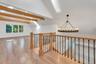 Vaulted ceilings featuring exposed timber beams, wood-finish flooring, a large circular wrought iron chandelier, and a custom stair railing with wood 