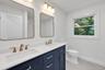 Double vanity with navy blue cabinetry, white stone-composite countertop, rectangular undermount sinks, brass-toned hardware, and dual rounded-edge mi
