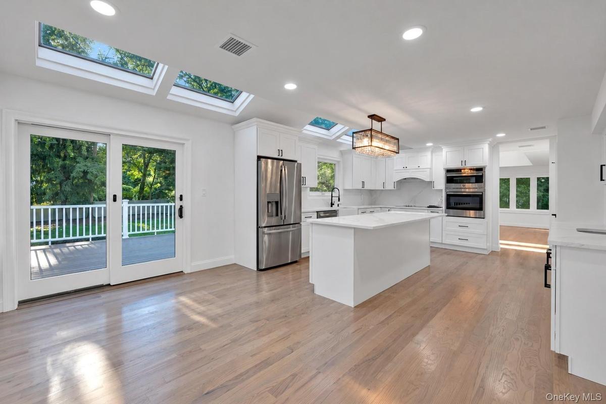 Kitchen featuring white cabinetry, central island with stone-finish countertop, stainless steel appliances, recessed ceiling lighting, and multiple sk