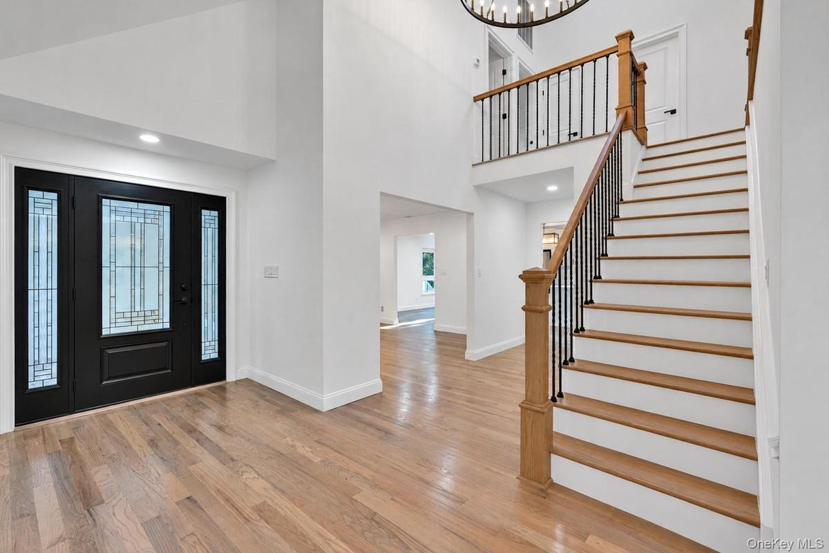 Foyer featuring a double-height ceiling, decorative glass-paneled door, wood-finish flooring, and a staircase with stained wood treads and metal balus
