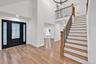 Foyer featuring a double-height ceiling, decorative glass-paneled door, wood-finish flooring, and a staircase with stained wood treads and metal balus