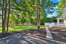Expansive backyard featuring a large grass lawn, mature trees, white wood railing deck, stone-bordered asphalt pathway, and privacy fencing