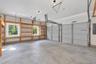 Multi-bay garage featuring dual pane windows, extensive built-in wood shelving, concrete flooring, and high-clearance overhead doors