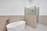 Freestanding white soaking tub with gold-tone floor-mounted faucet, walk-in glass shower enclosure, gold-tone shower fixtures, and neutral large-forma