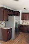 Dark wood-finish cabinetry, stainless steel refrigerator, neutral-toned solid surface countertops...