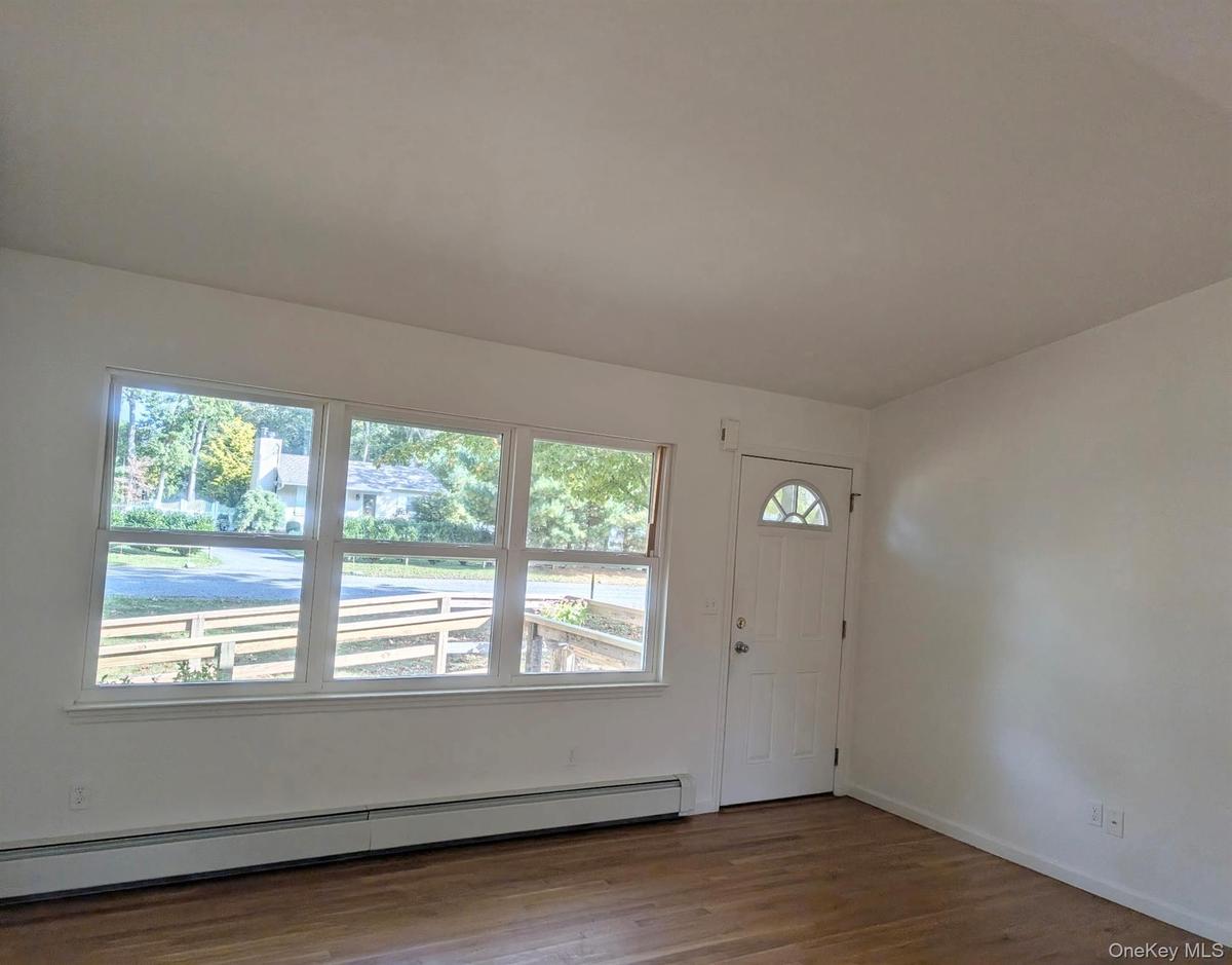 Interior space featuring expansive triple-pane windows, cathedral ceiling, wood floors, and a white entry door with a decorative glass insert.