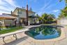 Free-form in-ground swimming pool with a diving board, surrounded by stone patio hardscaping, external brick chimney, and a detached storage structure