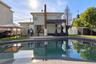 Exterior backyard featuring an in-ground swimming pool, concrete patio, red brick chimney, and white vinyl privacy fencing
