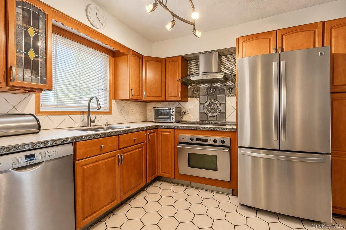 Kitchen featuring custom wood cabinetry, stainless steel appliances, a modern chimney-style range hood, hexagonal tile flooring, and a decorative tile