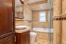 Bathroom featuring stone tile walls with diamond-pattern detailing, a built-in jetted tub, glass-enclosed shower, wood-finish vanity with a vessel sin