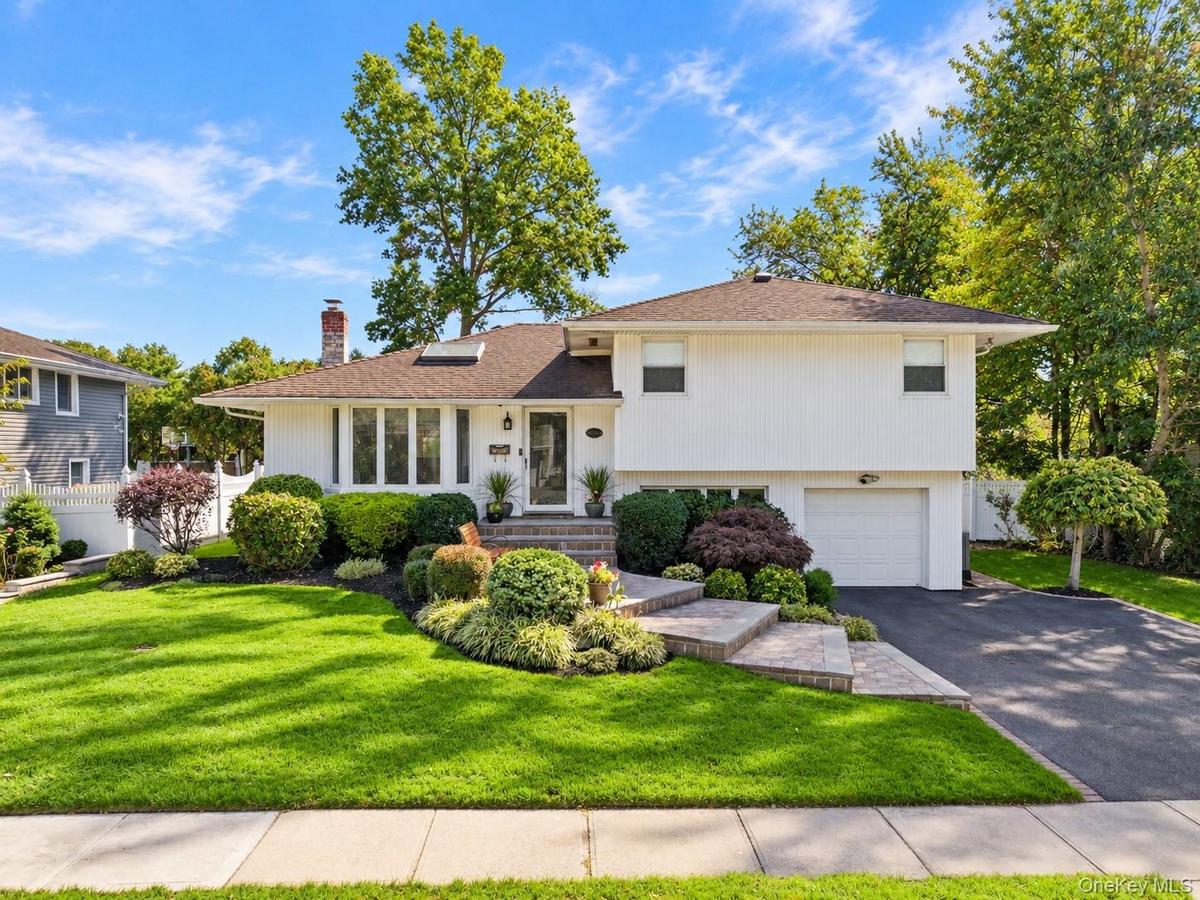 Split-level residence featuring vertical siding, brick chimney, stone-paver entryway stairs, attached garage, and manicured front landscaping