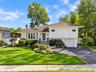 Split-level residence featuring vertical siding, brick chimney, stone-paver entryway stairs, attached garage, and manicured front landscaping