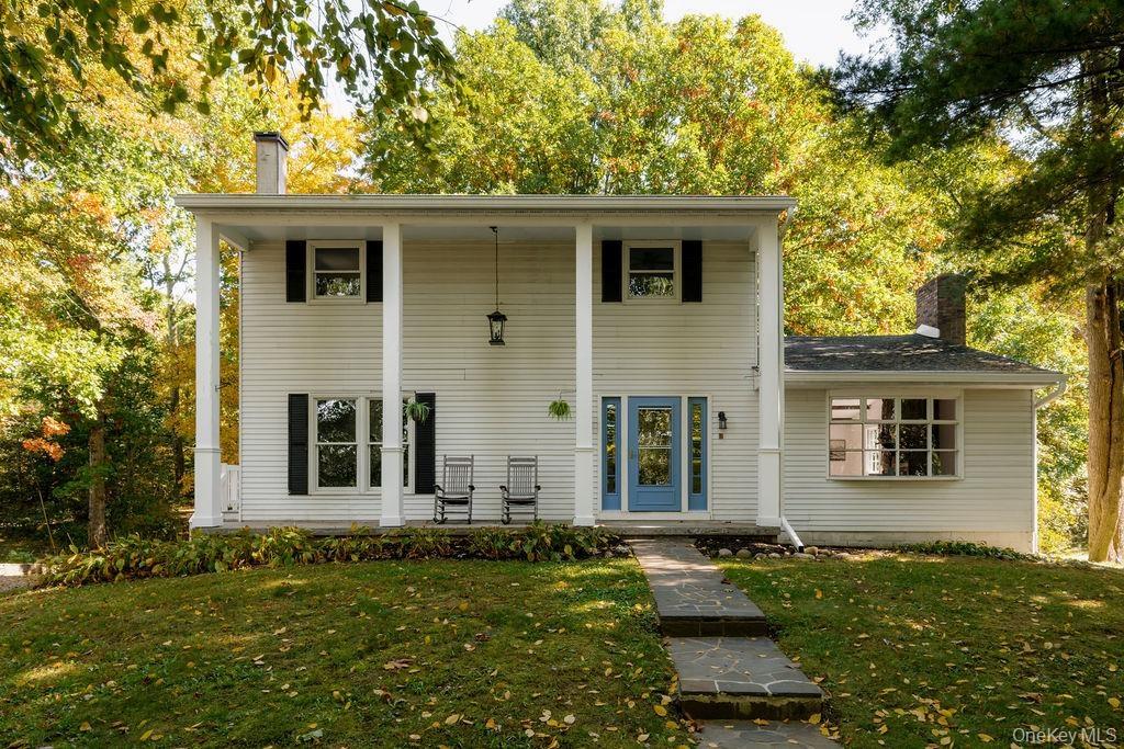 Two-story residence featuring a covered front porch with square columns, light-colored horizontal siding, dark window shutters, and a natural stone wa