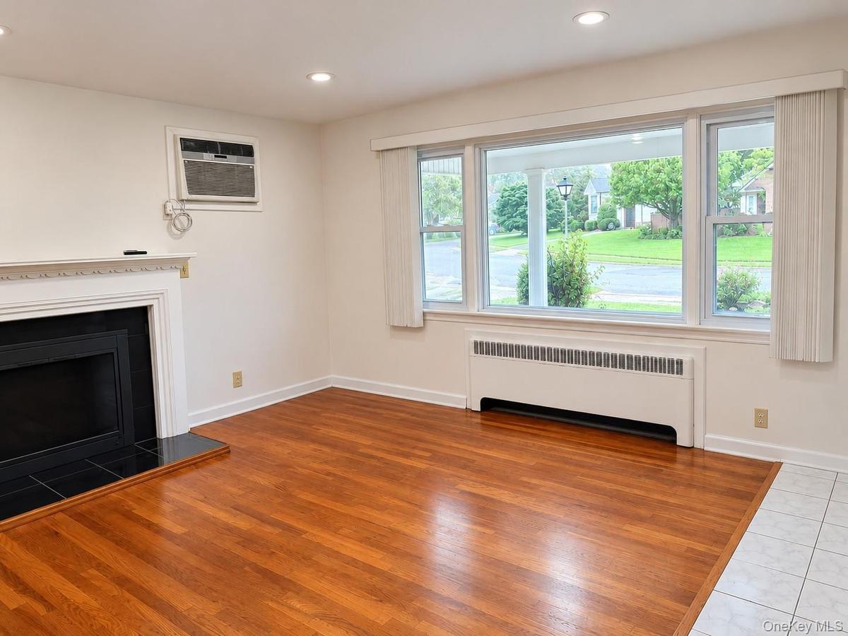 Hardwood flooring, white fireplace with a black tile hearth, window air conditioning unit, recessed lighting, and large picture windows