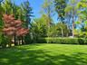 Expansive lawn surrounded by mature trees and a manicured hedge