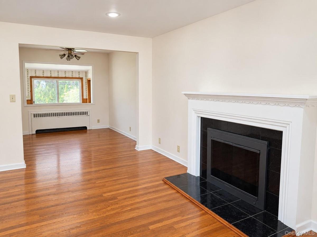 Hardwood flooring, fireplace with black tiled surround and hearth, white mantel, recessed lighting, and a ceiling fan in the adjoining space