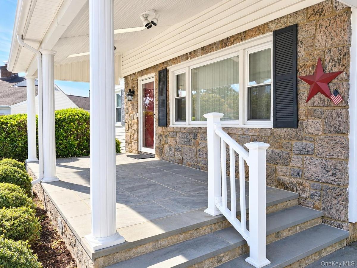 Covered front porch with skylights, stone facade, columns, bluestone stair and flooring, and a white railing with square balusters