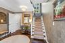 Foyer featuring patterned wallpaper, dark-stained wood flooring, a staircase with a central runner, a multi-pane fixed window, and crisp white millwor