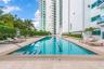 Lap pool with integrated steps, surrounded by a stone-tiled deck and lush green landscaping, set against a modern high-rise building