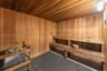 Wood-paneled sauna featuring a slatted wood ceiling, a built-in wood bench, and a sauna heater with stones