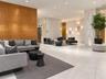 Spacious common area featuring textured accent wall, light stone tile flooring, and modern wall sconces
