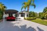 Exterior featuring a covered carport, painted masonry facade, screened-in entry, and mature landscaping