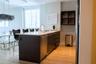 Kitchen island featuring dark-toned cabinetry, light-toned stone-finish countertop, integrated stainless steel dishwasher, and arched faucet