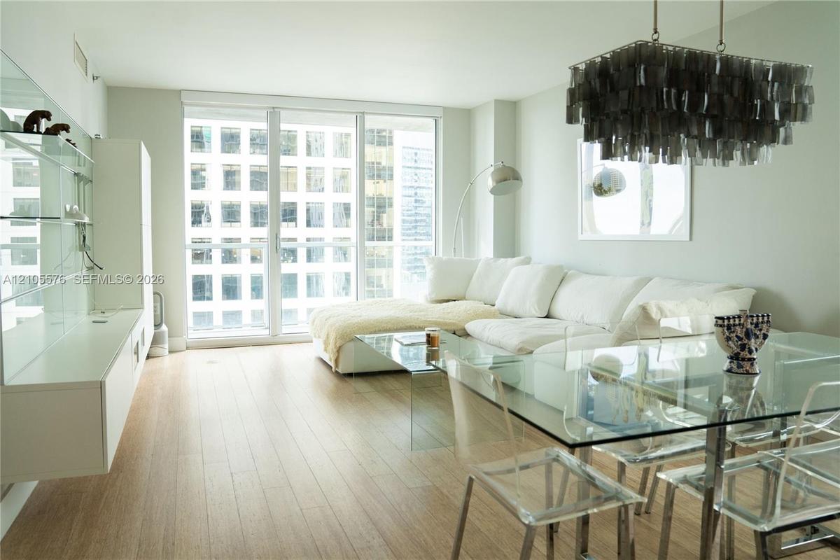 Floor-to-ceiling windows, wood-finish flooring, built-in wall cabinetry, and a decorative multi-tiered pendant light fixture