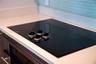 Black glass cooktop set into a white solid-surface countertop with a light blue glass subway tile backsplash