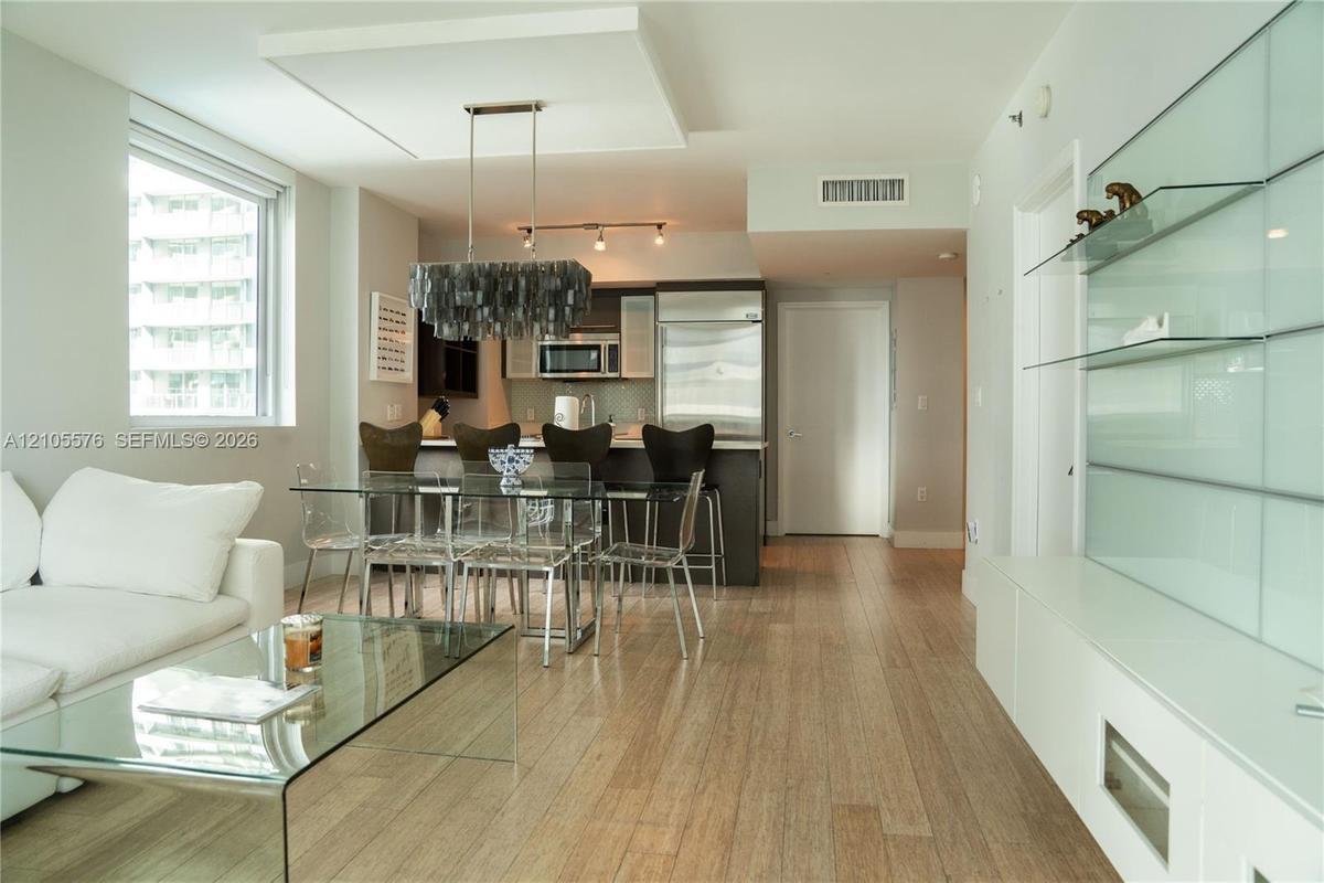 Open-concept interior featuring light wood-finish flooring, a contemporary island kitchen, built-in frosted glass shelving, and a decorative drop-pend