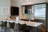 Kitchen featuring dark wood-finish cabinetry, light-toned stone countertops, a glass tile backsplash, stainless steel appliances, and an integrated br