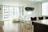 Open-concept living space featuring wood-finish flooring, floor-to-ceiling windows, built-in wall-mounted cabinetry, a central island with a solid sur
