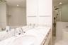 Dual-sink vanity with stone-finish countertops, polished chrome faucets, a full-width wall mirror, and a glass-enclosed shower with a rainfall showerh