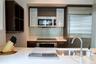 Kitchen featuring dark wood cabinetry, glass-front upper cabinets, stainless steel appliances, light-toned solid surface countertops, and a glass tile