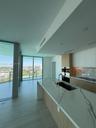 Kitchen featuring a waterfall-edge island with stone-finish countertops, flat-panel cabinetry, built-in stainless steel appliances, and floor-to-ceili