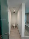 Enclosed water closet featuring a high-efficiency toilet, neutral stone-finish flooring, frosted glass door, and recessed lighting