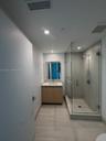 Bathroom featuring wood-finish cabinetry, a rectangular undermount sink, a glass-enclosed shower with full-height tile surround, and large-format floo