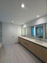 Double vanity featuring light-toned wood cabinetry, dual undermount sinks, stone-finish countertops, wall-to-wall integrated mirror with vertical LED 
