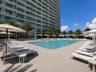 Swimming pool with light-colored paver decking, surrounding palm trees, and glass-railing balconies on the high-rise exterior