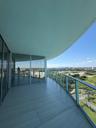 Expansive covered terrace featuring large-format tile flooring, curved architecture, and a glass-paneled railing