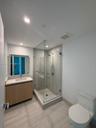 Bathroom featuring a wood-finish vanity with a stone countertop, an integrated rectangular sink, a glass-enclosed shower with large-format wall tile, 