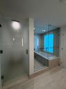 Frosted glass shower enclosure, deep soaking tub with a tiled surround, glass partition walls, and large-format tile flooring