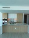 Kitchen featuring wood-finish cabinetry, waterfall island with stone countertop, integrated refrigerator, built-in double oven, and stone-finish backs