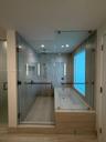 Wet room featuring a glass-enclosed shower, soaking tub, recessed wall niche, wall-mounted shower hardware, and stone-finish wall and floor tiling