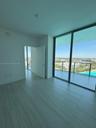 Floor-to-ceiling glass windows, neutral tile flooring, and a private balcony featuring a glass railing