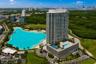 High-rise residential tower featuring a tiered podium with multiple swimming pools, expansive man-made lagoon, and tropical landscaping