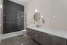 Floating vanity with a white vessel sink, polished countertop, circular mirror, and floor-to-ceiling dark tile accent wall