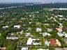 Aerial perspective of a lush, wooded residential area featuring mature tree canopy, dense vegetation, and a cityscape skyline in the distance